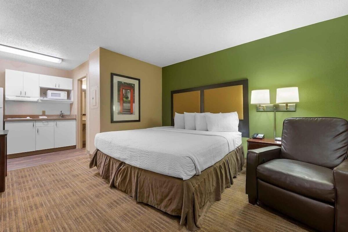 Une chambre d’hôtel avec un lit, une chaise, un bureau, un four à micro-ondes et un tableau au mur.