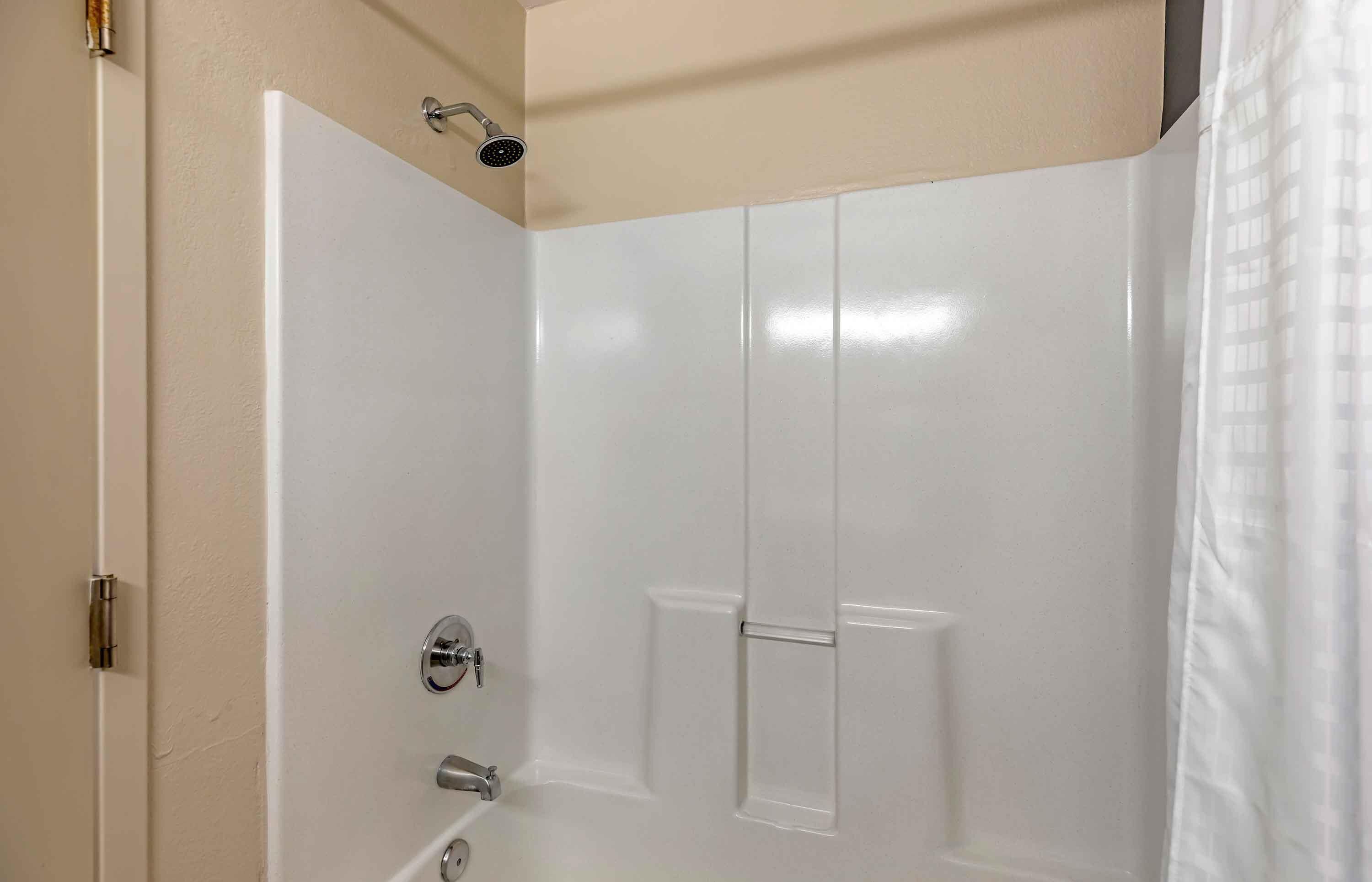 A small, enclosed shower area with a white door, a showerhead, and a curtain.