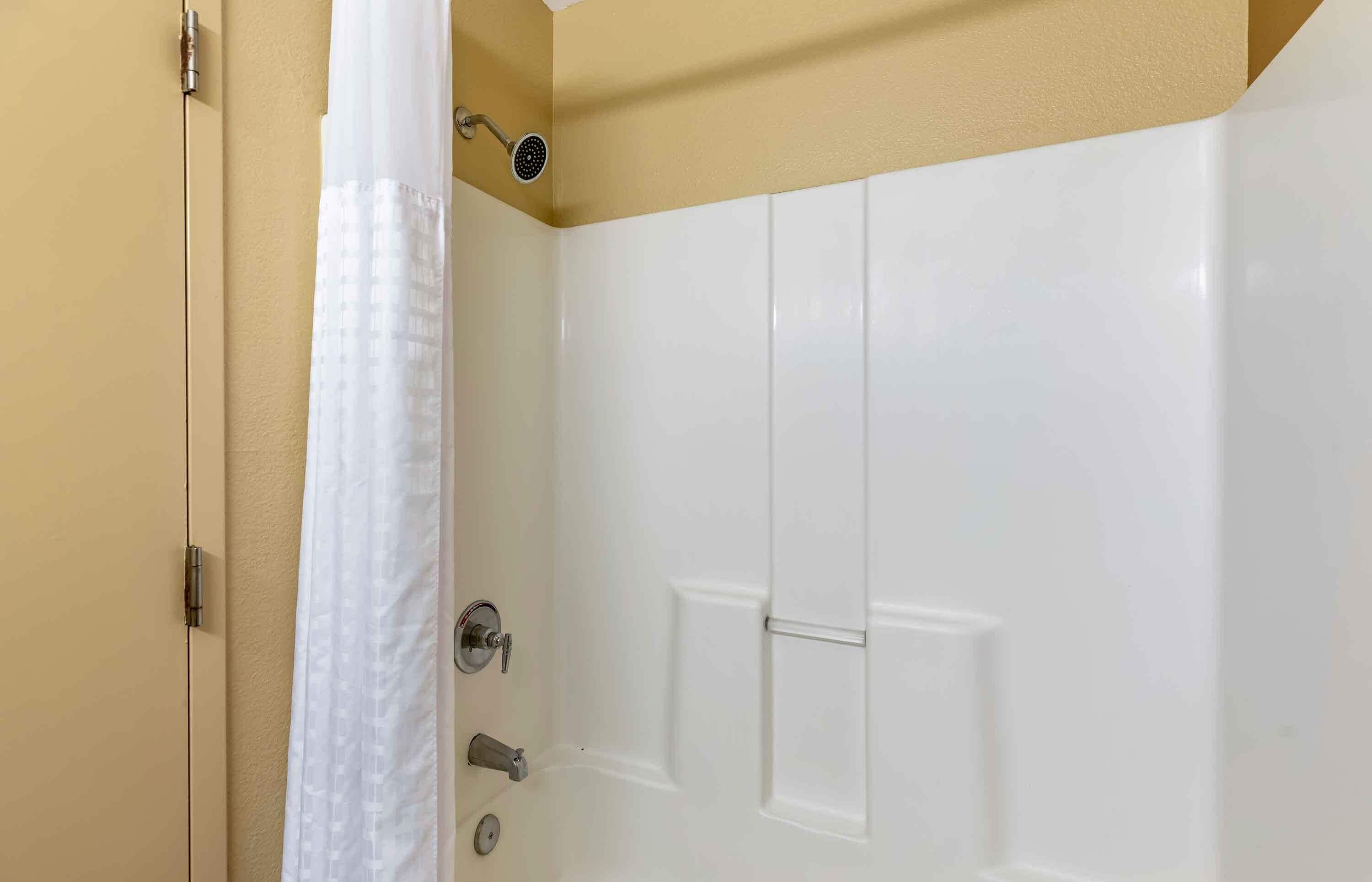 A bathroom with a white door, a shower curtain, and a showerhead.
