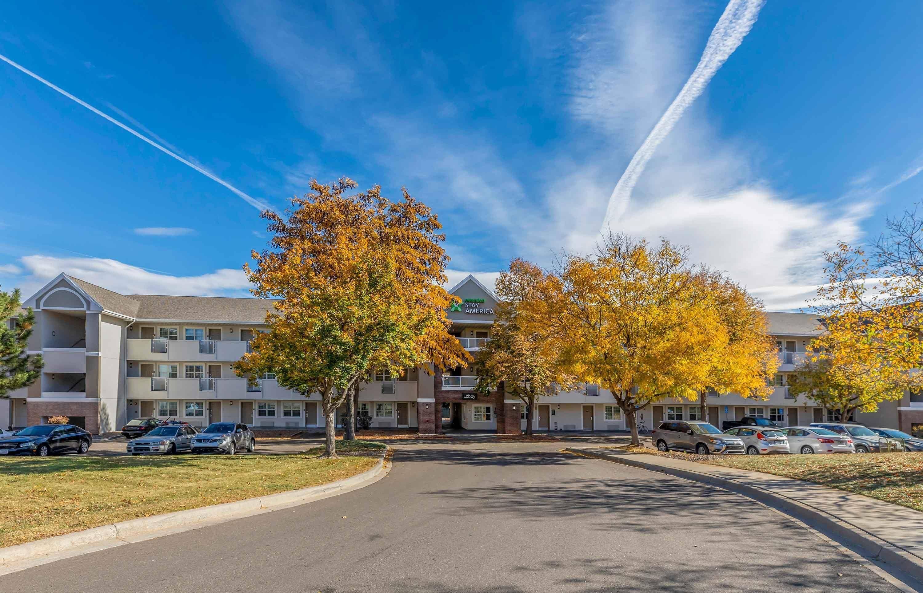 A multi-story motel with a central lobby, parking lot, and autumn foliage.