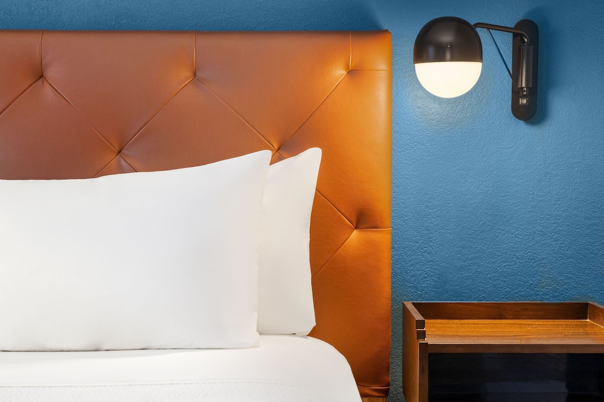 A bed with a tufted headboard, a bedside table, and a wall-mounted lamp.