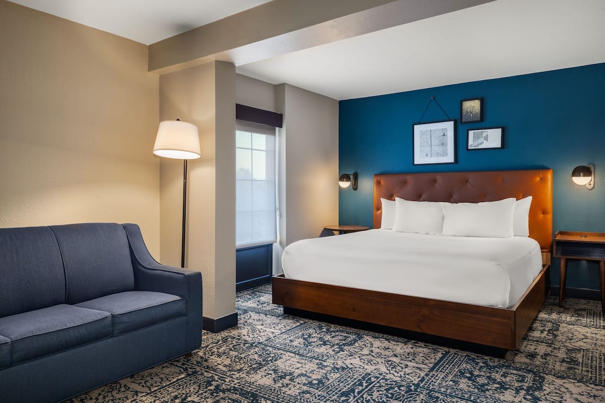 A hotel room with a bed, a sofa, a lamp, and a patterned rug.