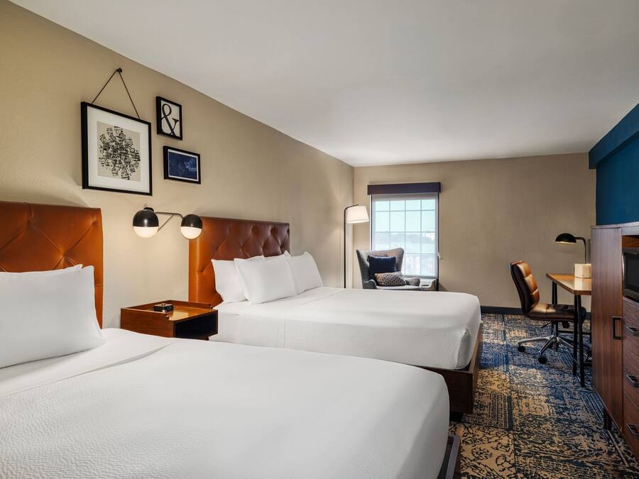 A hotel room with two beds, a desk, a chair, a TV, and a window.