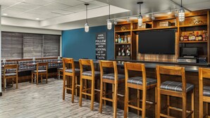 A bar area with wooden bar stools, a counter with a television, and shelves with bottles.