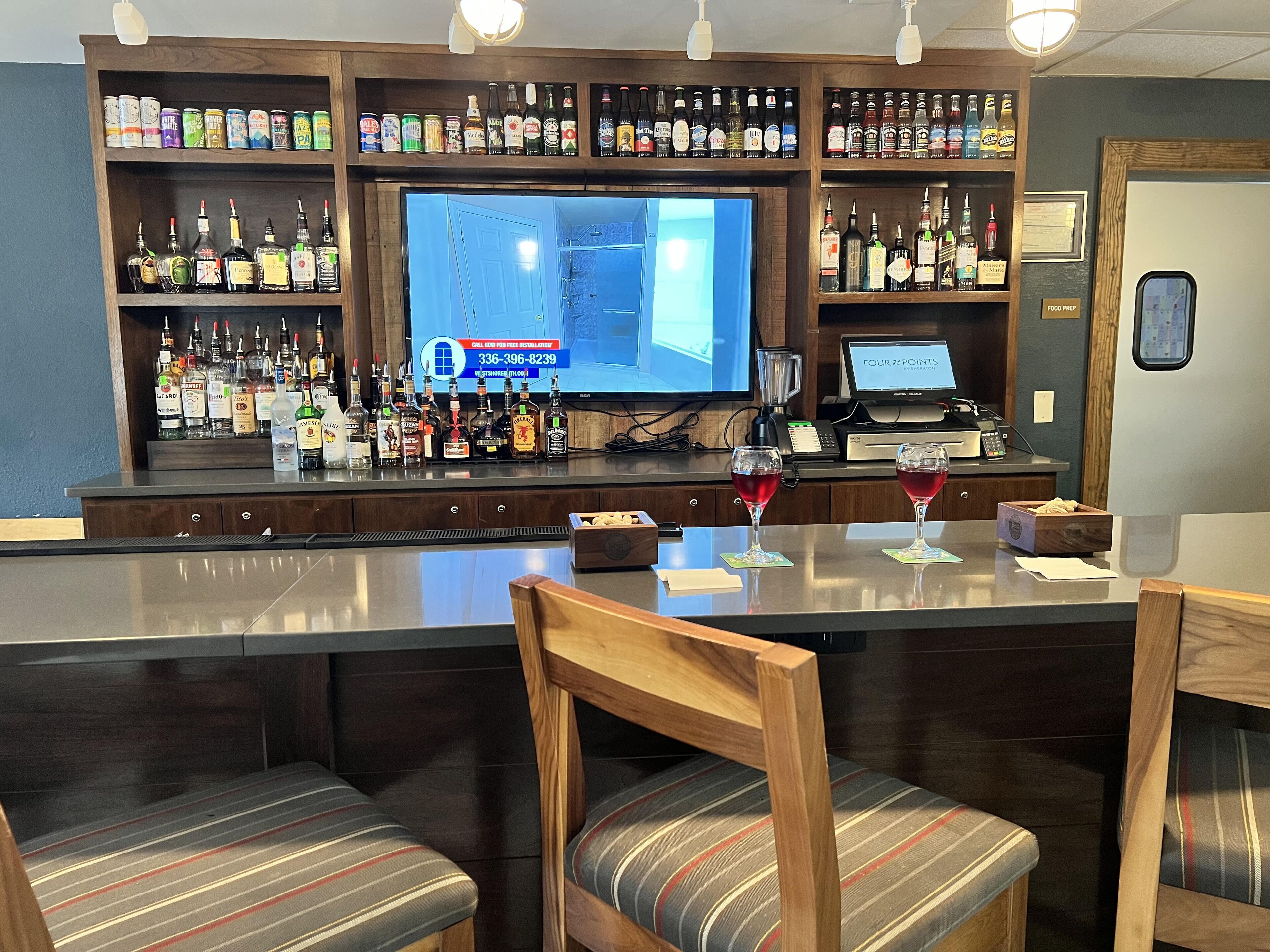A bar area with multiple liquor bottles, a television screen, and seating with striped cushions.