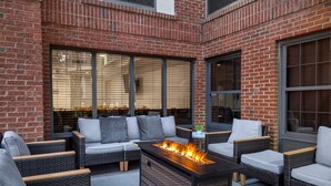 An outdoor seating area with wicker furniture, a fire feature, and large windows. - Four Points by Sheraton Greensboro Airport (Greensboro)