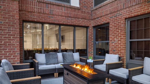 An outdoor seating area with wicker furniture, a fire feature, and large windows.