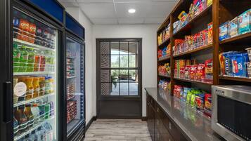 A corridor with a refrigerated beverage display, snack shelves, and a view through a door.