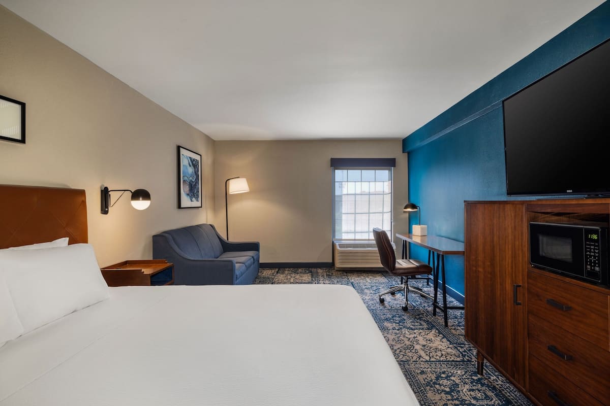 A hotel room with a large bed, a desk with a chair, a television, and a microwave.