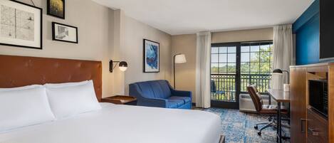Een hotelkamer met een groot bed, een bureau, een stoel en uitzicht op het omliggende landschap door een schuifdeur.
