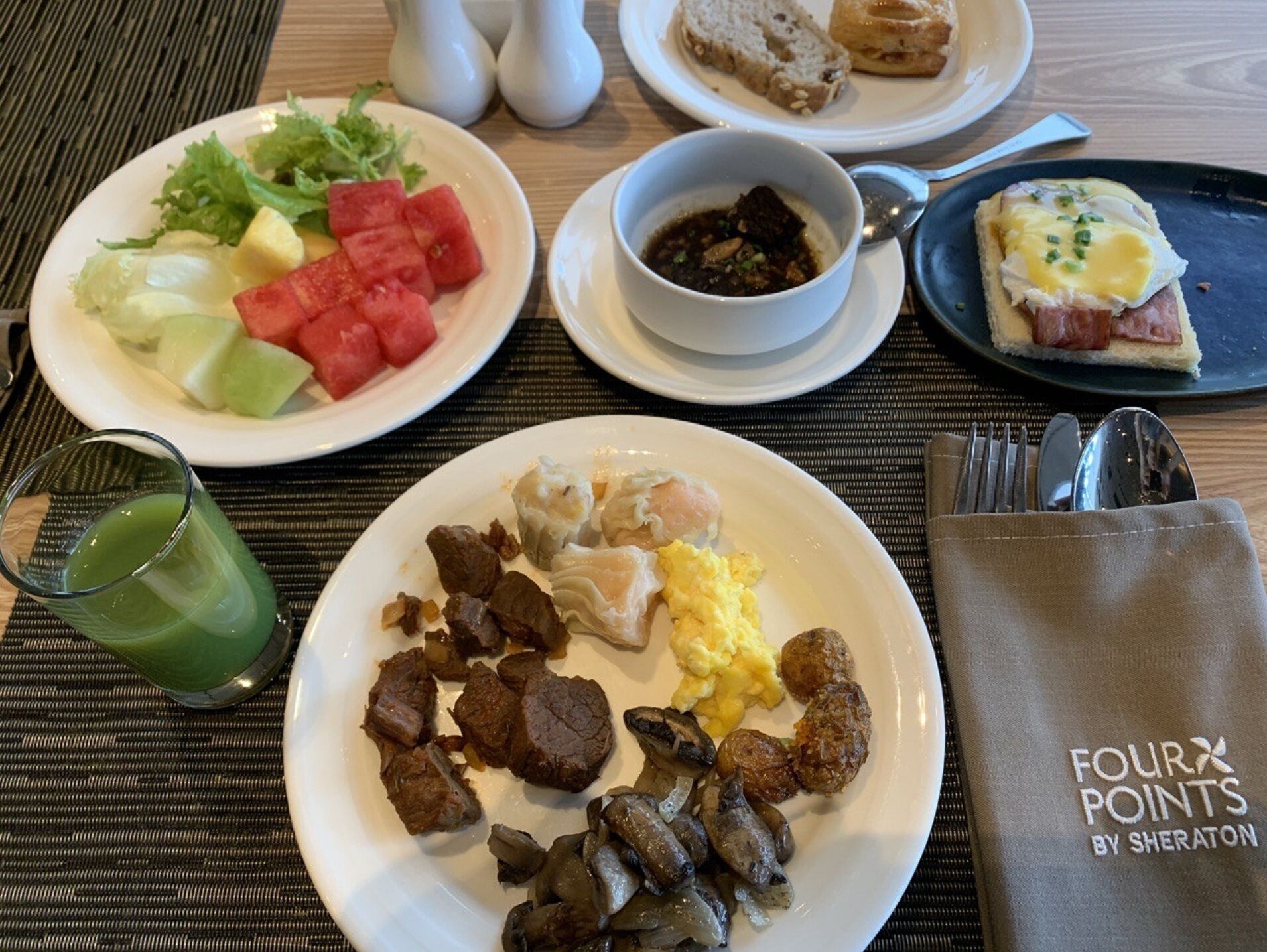 Ein Frühstückstisch mit Speisen, einem Glas grünes Getränk und einer Serviettenverpackung mit der Aufschrift "FOUR POINTS BY SHERATON".