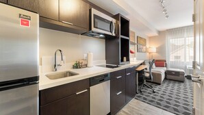 A modern kitchen with a built-in refrigerator, microwave, and dishwasher. There is a dining area with a table and chairs, and a sofa. - TownePlace Suites by Marriott Greensboro Coliseum Area (Greensboro)