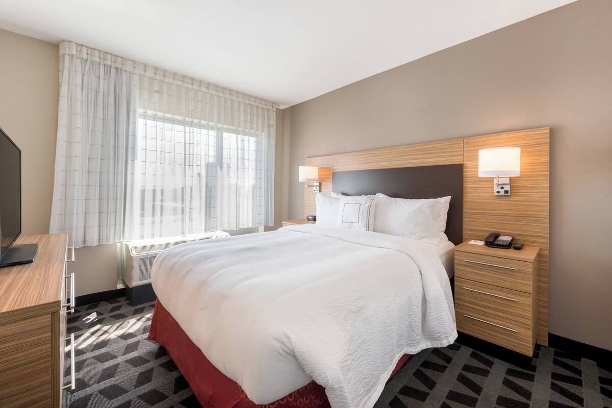 Une chambre d’hôtel avec un grand lit, des lampes de chevet, un bureau et une fenêtre avec des rideaux.