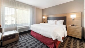 A hotel room with a large bed, a bedside table, a lamp, and a window with curtains. - TownePlace Suites by Marriott Greensboro Coliseum Area (Greensboro)
