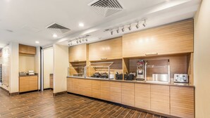 A modern kitchen area with wooden cabinets, stainless steel appliances, and a tiled floor. - TownePlace Suites by Marriott Greensboro Coliseum Area (Greensboro)