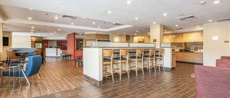 A spacious indoor area with a long counter and multiple chairs, a kitchen area, and a seating area with tables and chairs.
