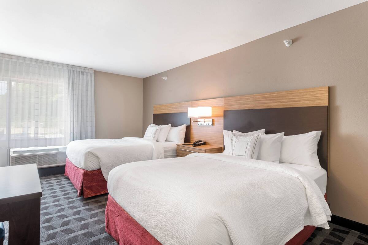 Une chambre d’hôtel avec deux lits, un bureau et une fenêtre avec des rideaux légers.
