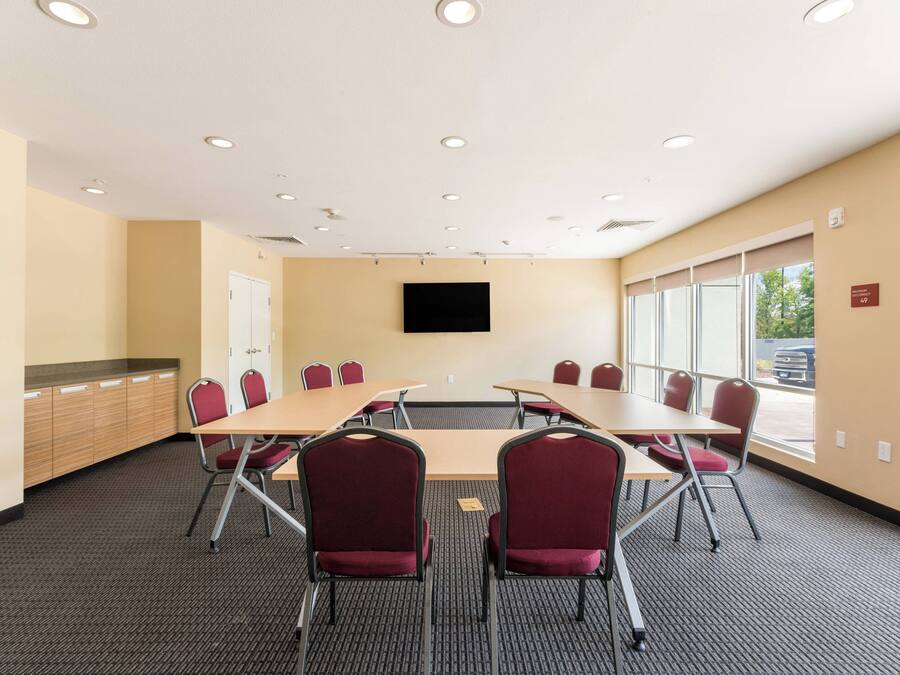 A conference room with a long table, red chairs, a flat-screen TV, and large windows.