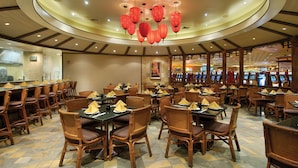 A restaurant with round tables and wicker chairs, a ceiling with red lanterns, and a visible exit sign. - Gold Coast Hotel and Casino (Las Vegas)