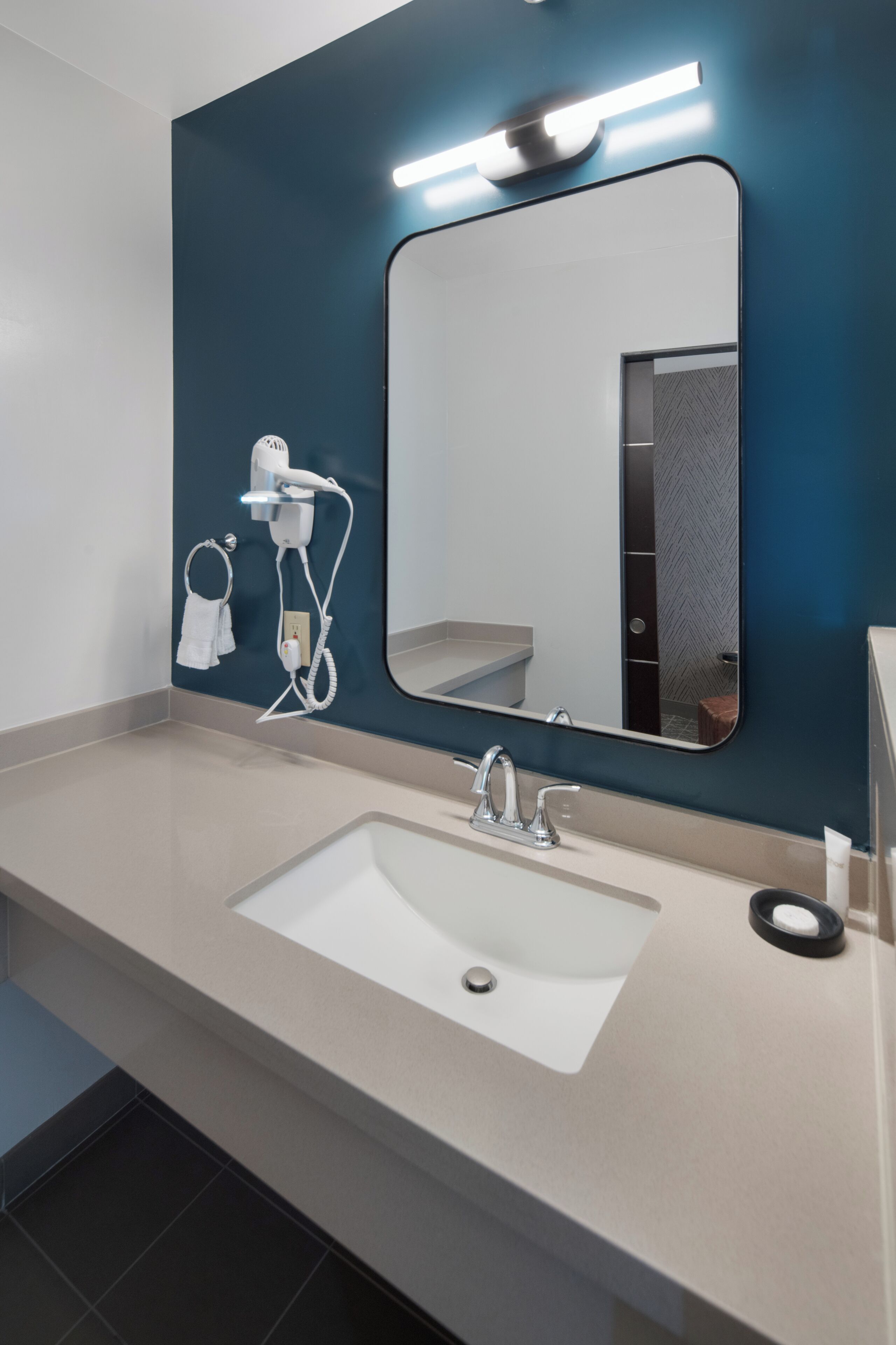 Une salle de bain moderne avec un grand miroir, un lavabo et un sèche-cheveux fixé au mur.
