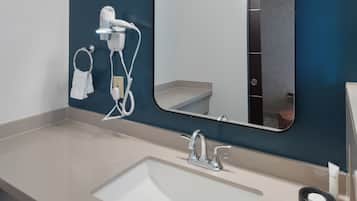 Une salle de bain moderne avec un grand miroir, un lavabo et un sèche-cheveux fixé au mur.