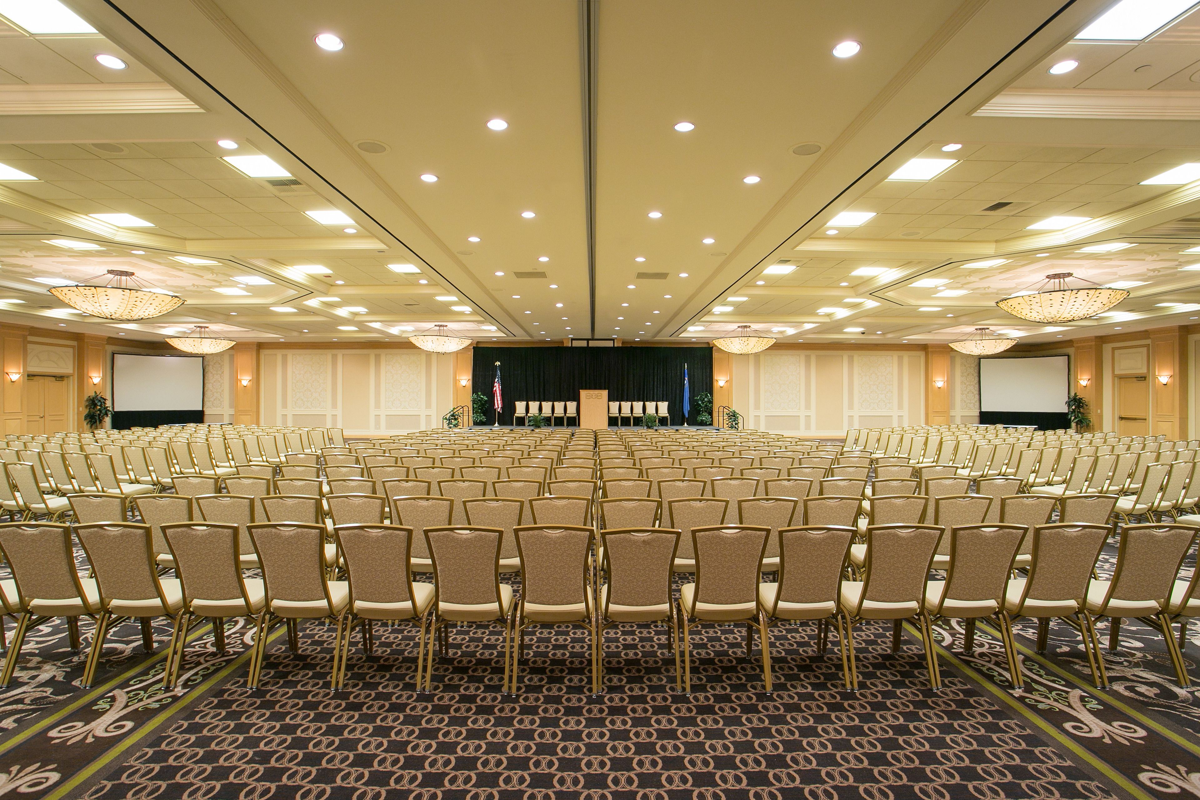 A conference room with rows of chairs, a stage, and a projector screen.