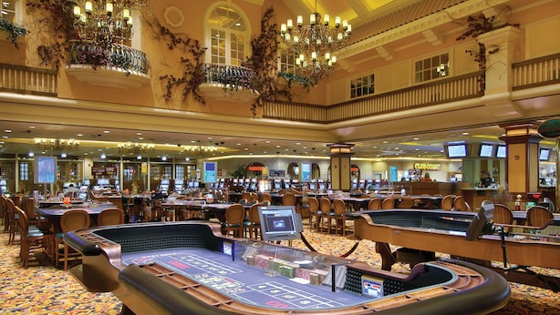 A casino with multiple blackjack tables, a large chandelier, and a buffet area in the background. - Gold Coast Hotel and Casino (Las Vegas)