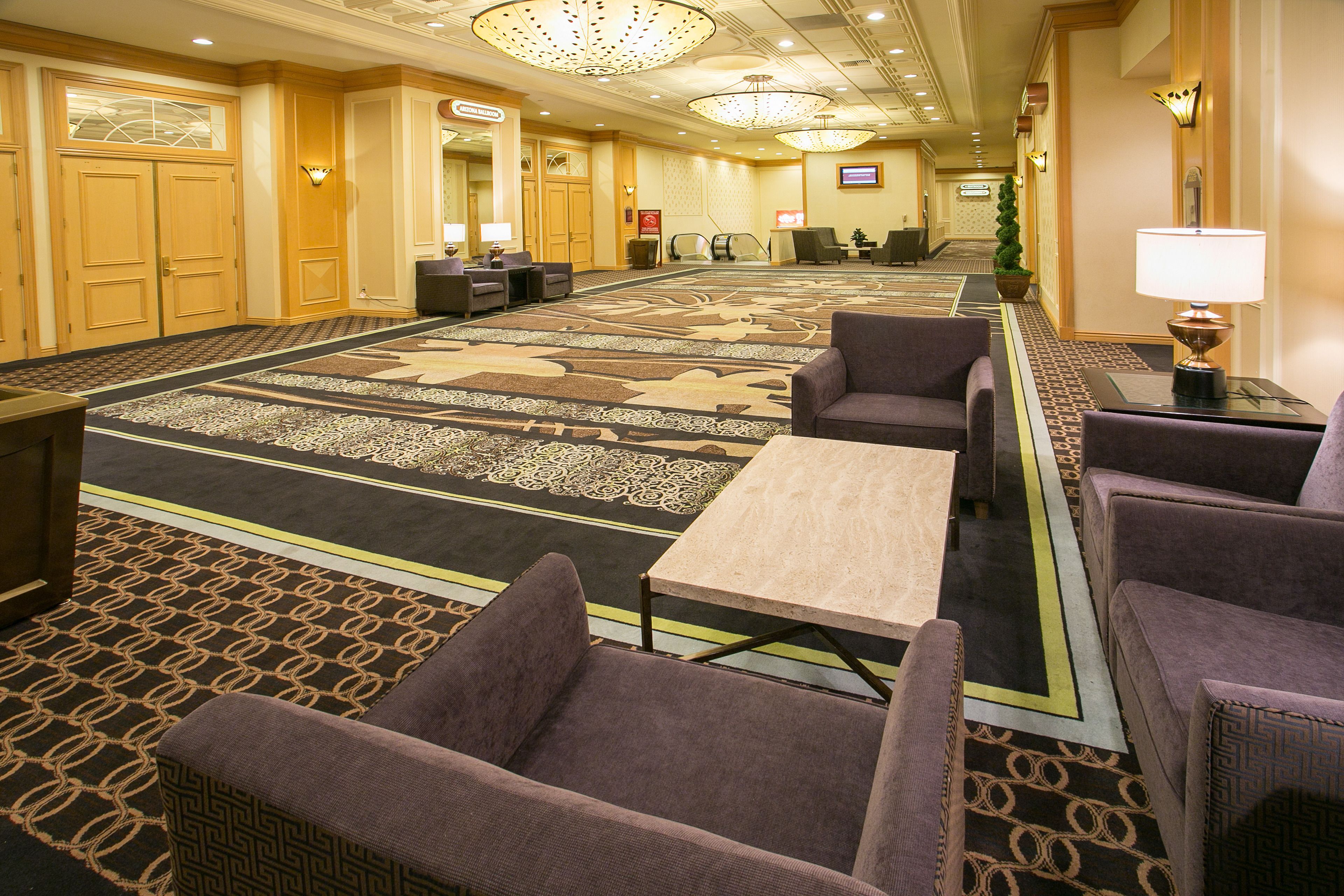 A hotel lobby with a carpeted floor, seating area with chairs, a reception desk, and a television screen.