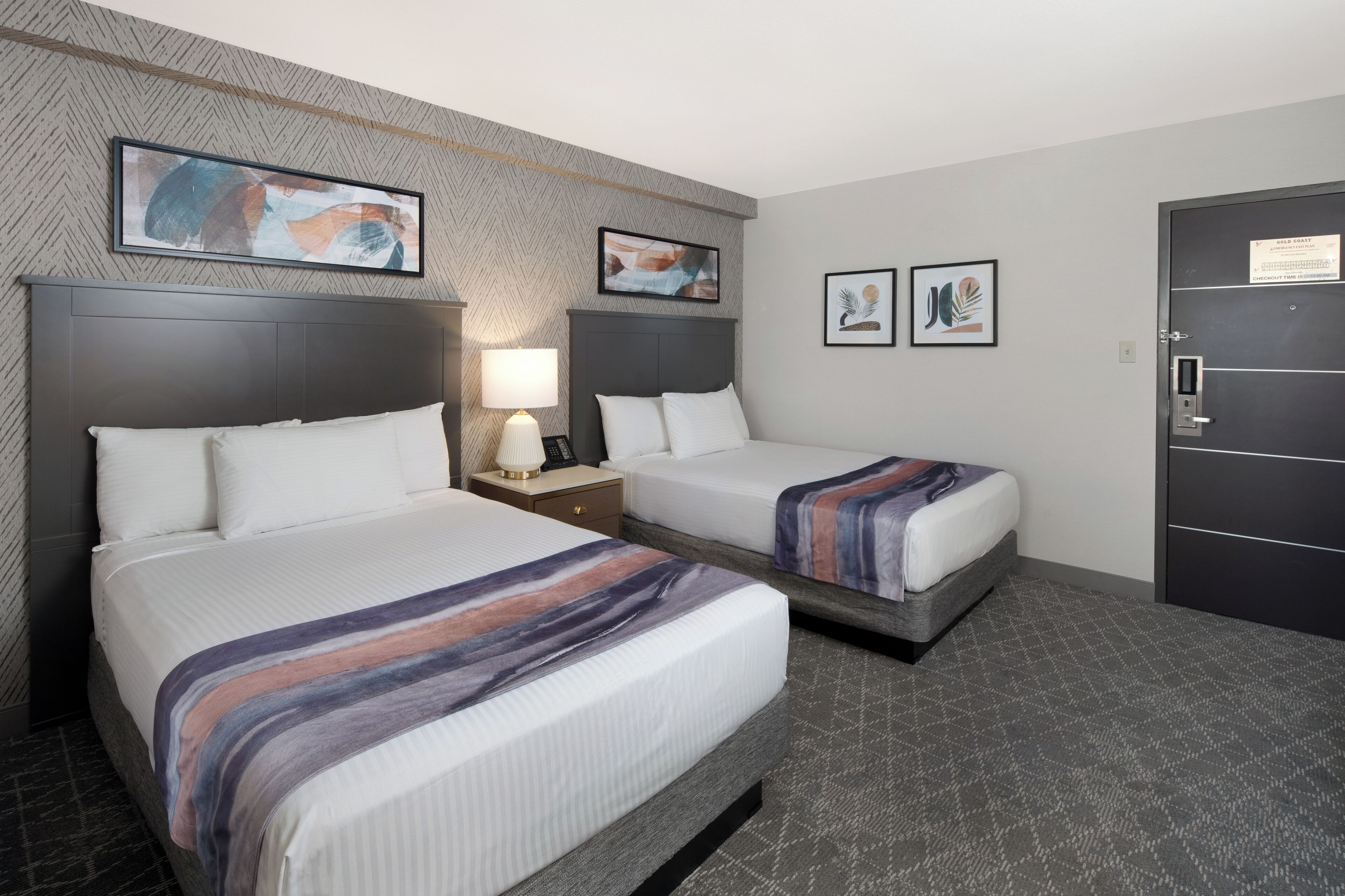 A hotel room with two beds, a nightstand with a lamp, and a door with a lock.