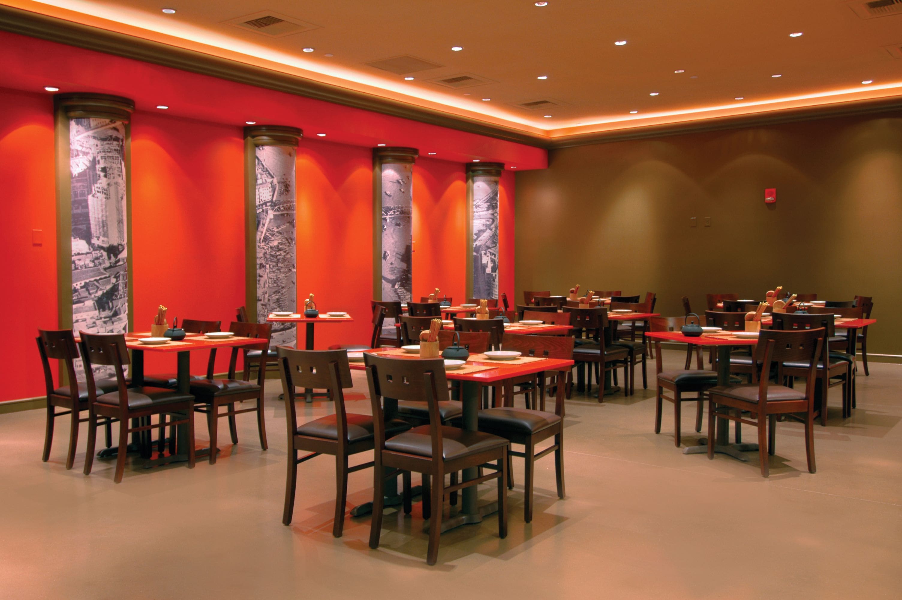 Un restaurant doté de nombreuses tables et chaises, de murs rouges et de colonnes décoratives.