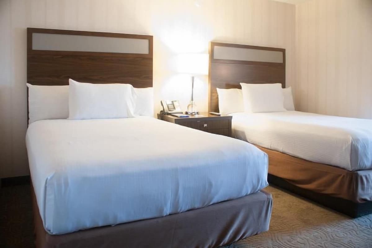 Een hotelkamer met twee bedden, een nachtkastje met een lamp en een aan de muur bevestigde telefoon.