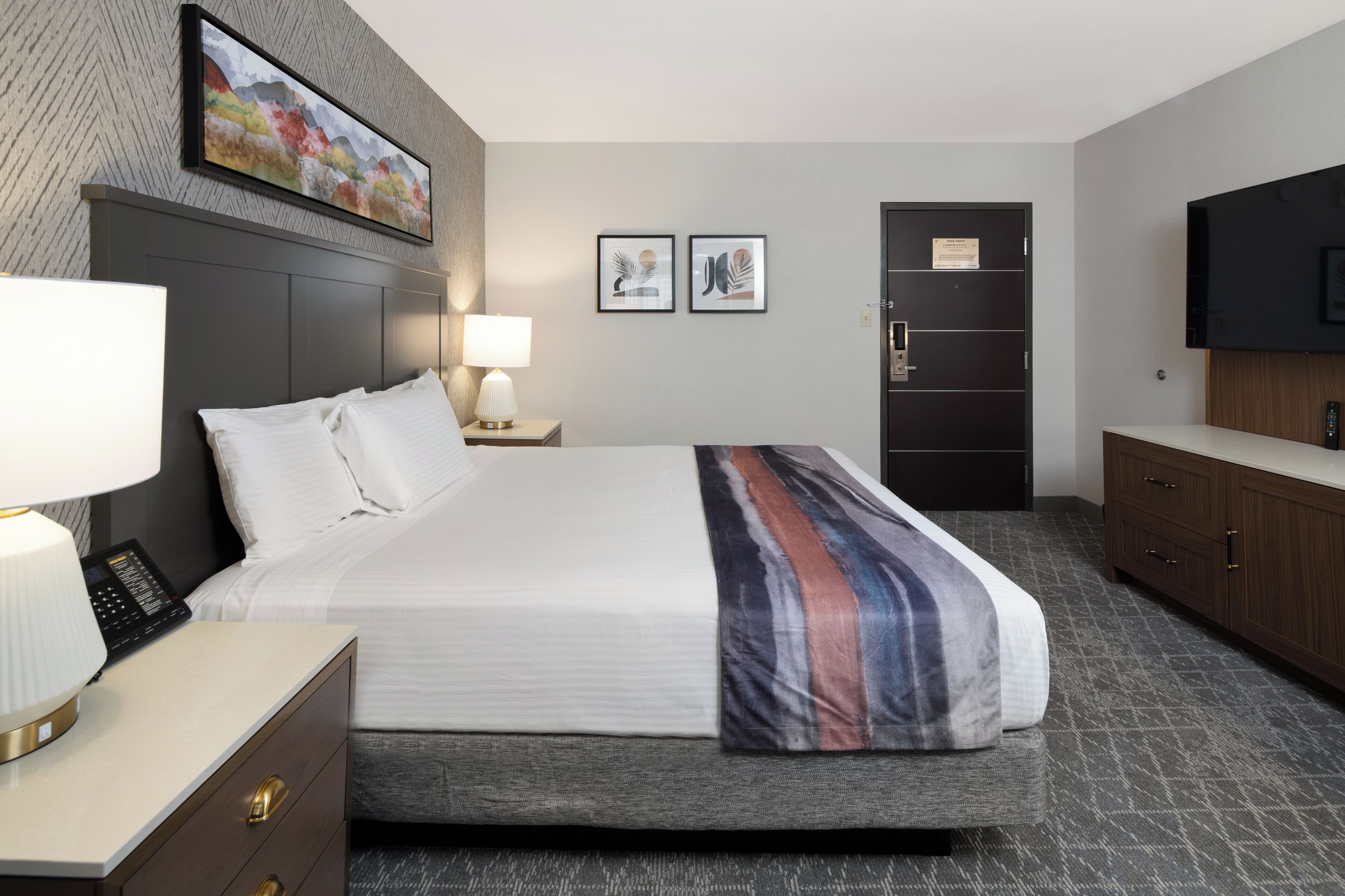 A hotel room with a large bed, bedside tables, a TV, and artwork on the walls.