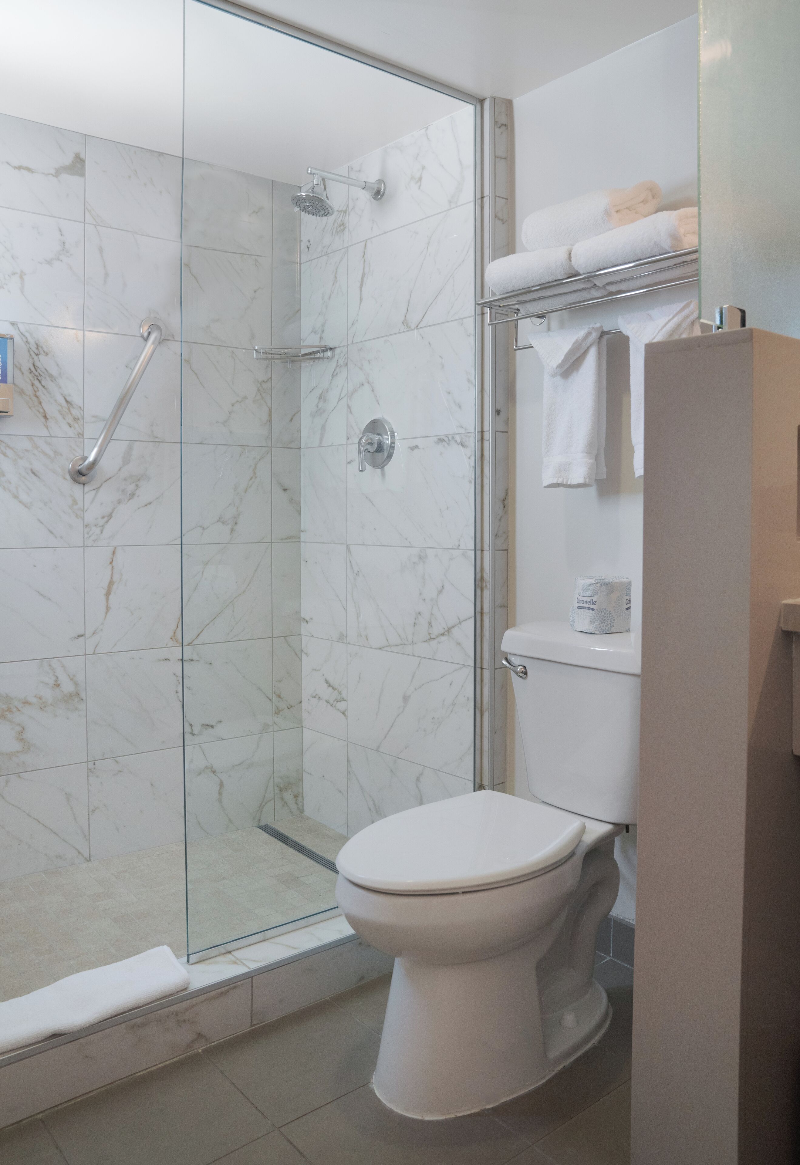 Un baño con ducha de vidrio, inodoro blanco y toallero con toallas dobladas.