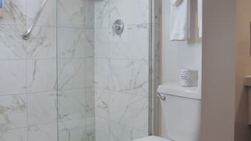 Ein Badezimmer mit einer Duschkabine, einer weißen Toilette und einem Handtuchhalter mit gefalteten Handtüchern.