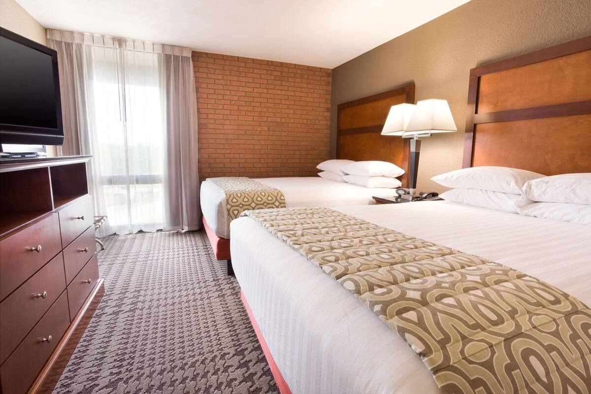 A hotel room with a large bed, a TV, a dresser, and a brick wall.