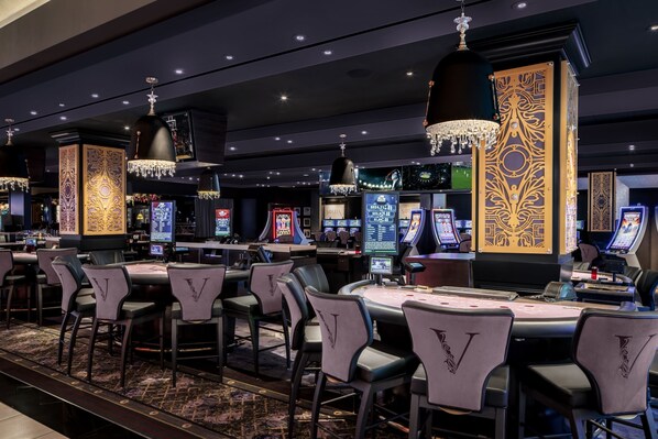 A casino with multiple gaming tables, chairs, and slot machines.