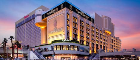 A multi-story hotel with a prominent sign, a curved entrance, and a large parking area.