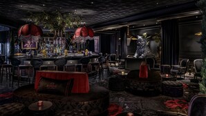 A bar area with round tables, cushioned seating, and a large red umbrella. - The Vanderpump Las Vegas Hotel Casino - A Caesars Rewards Destination (Las Vegas)