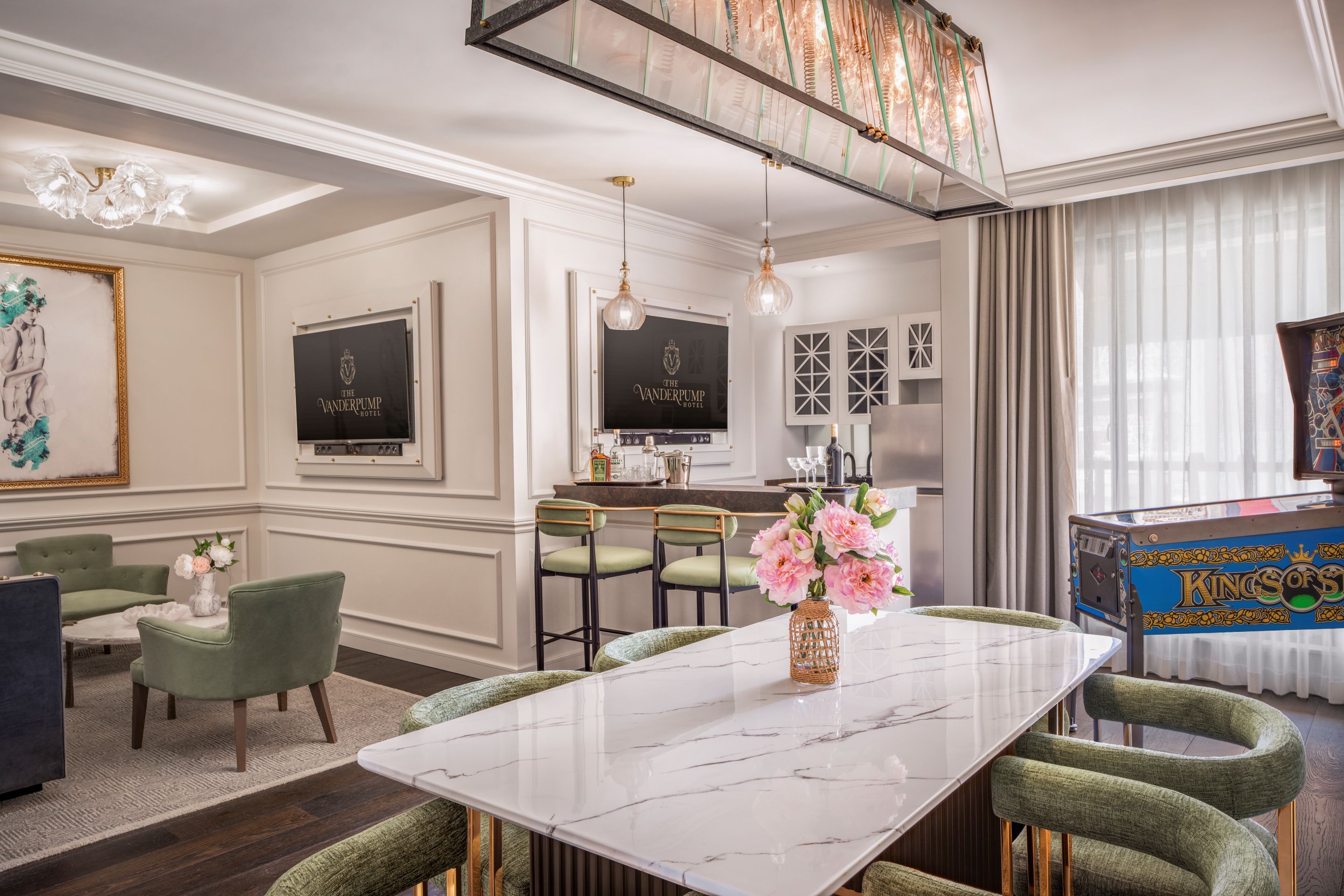 Un hall d’hôtel avec un comptoir de réception en marbre, des fauteuils à revêtement vert, un grand tableau et un lustre.