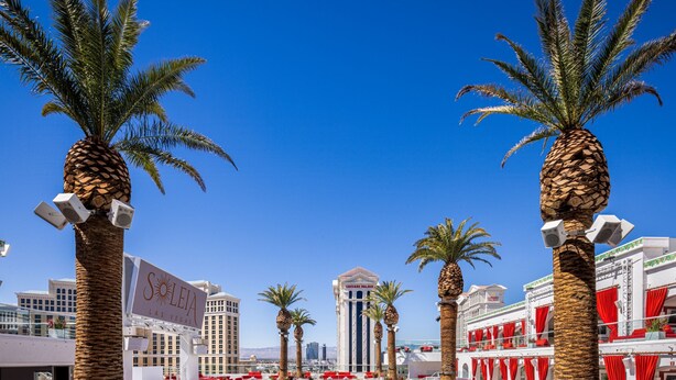 A pool area with palm trees, a clear blue sky, and a casino building in the background. - The Vanderpump Las Vegas Hotel Casino - A Caesars Rewards Destination (Las Vegas)