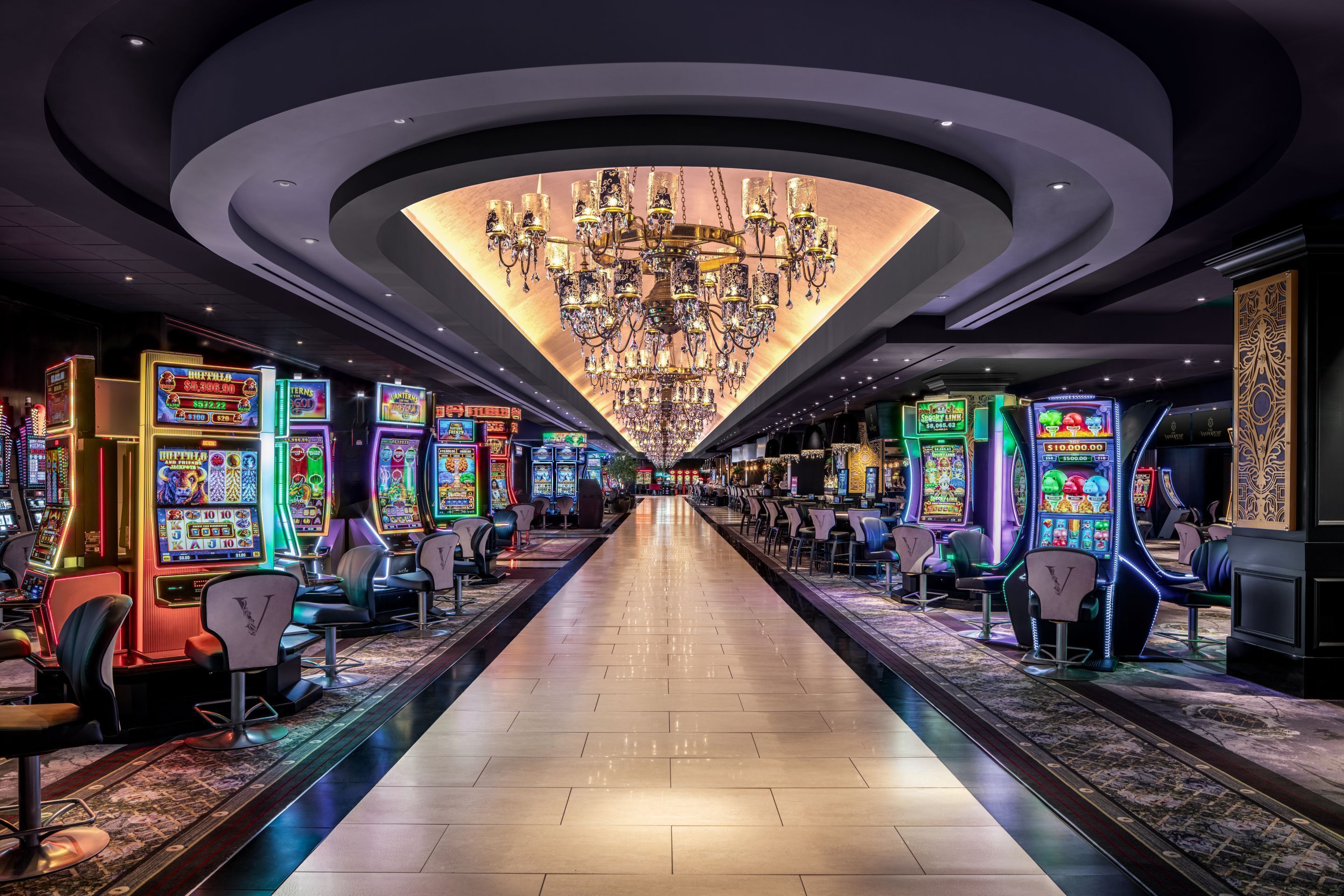 A casino with a long corridor lined with slot machines and a large chandelier.