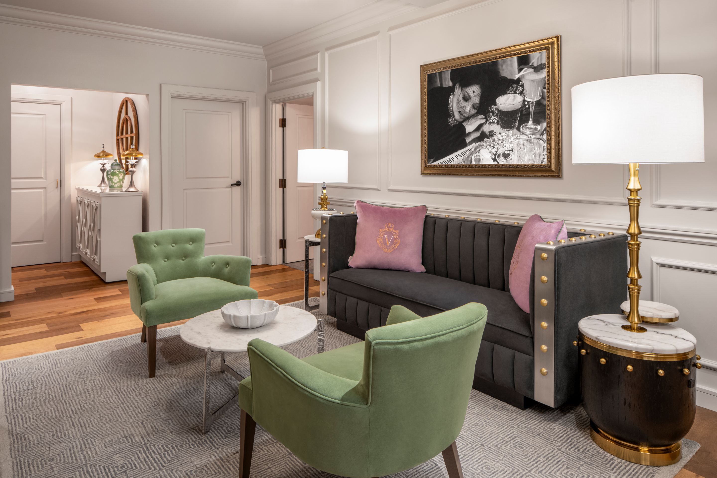 A room with a green sofa, two green armchairs, a round coffee table, and a side table with a lamp.