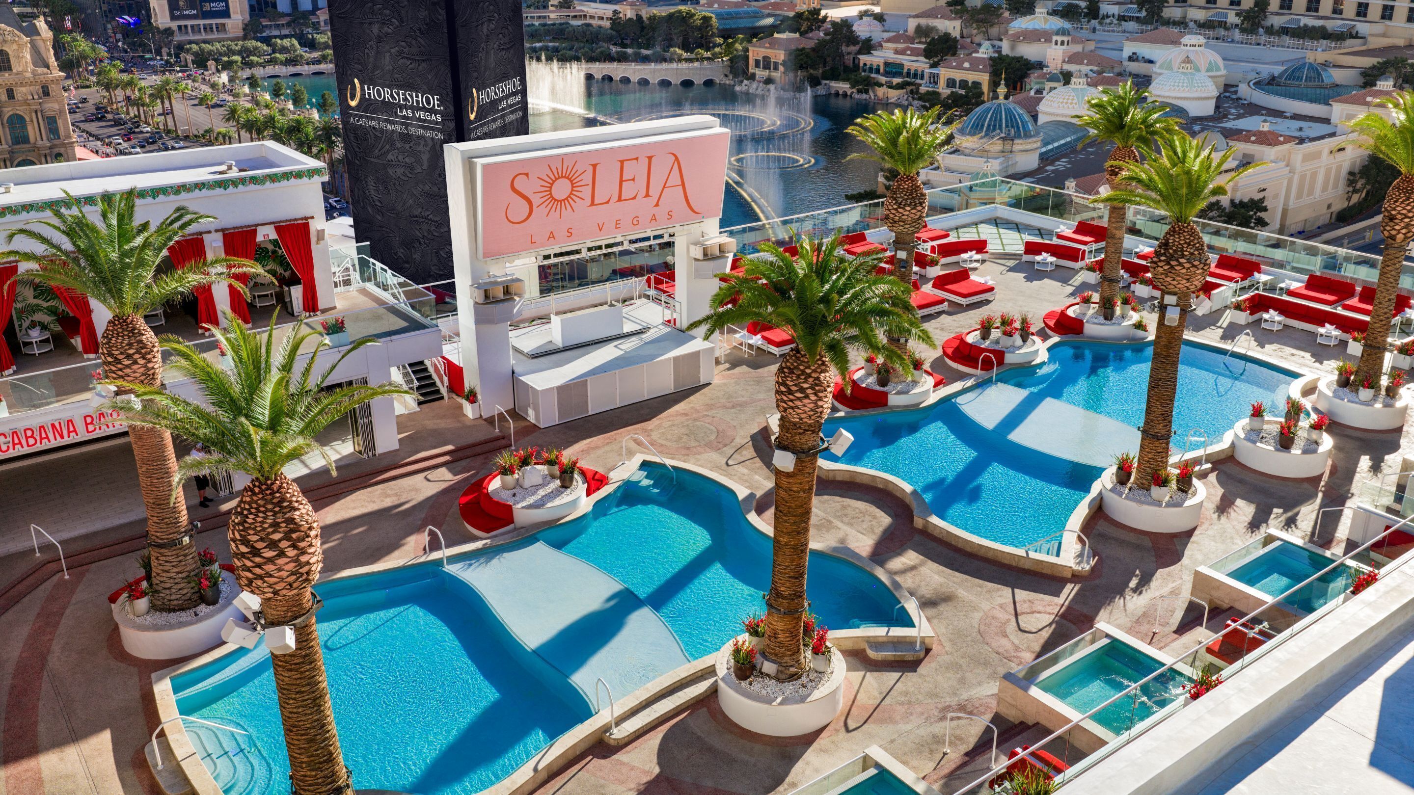 A rooftop pool area with multiple swimming pools, palm trees, and a large sign for 'LEIA LAS VEGAS'.