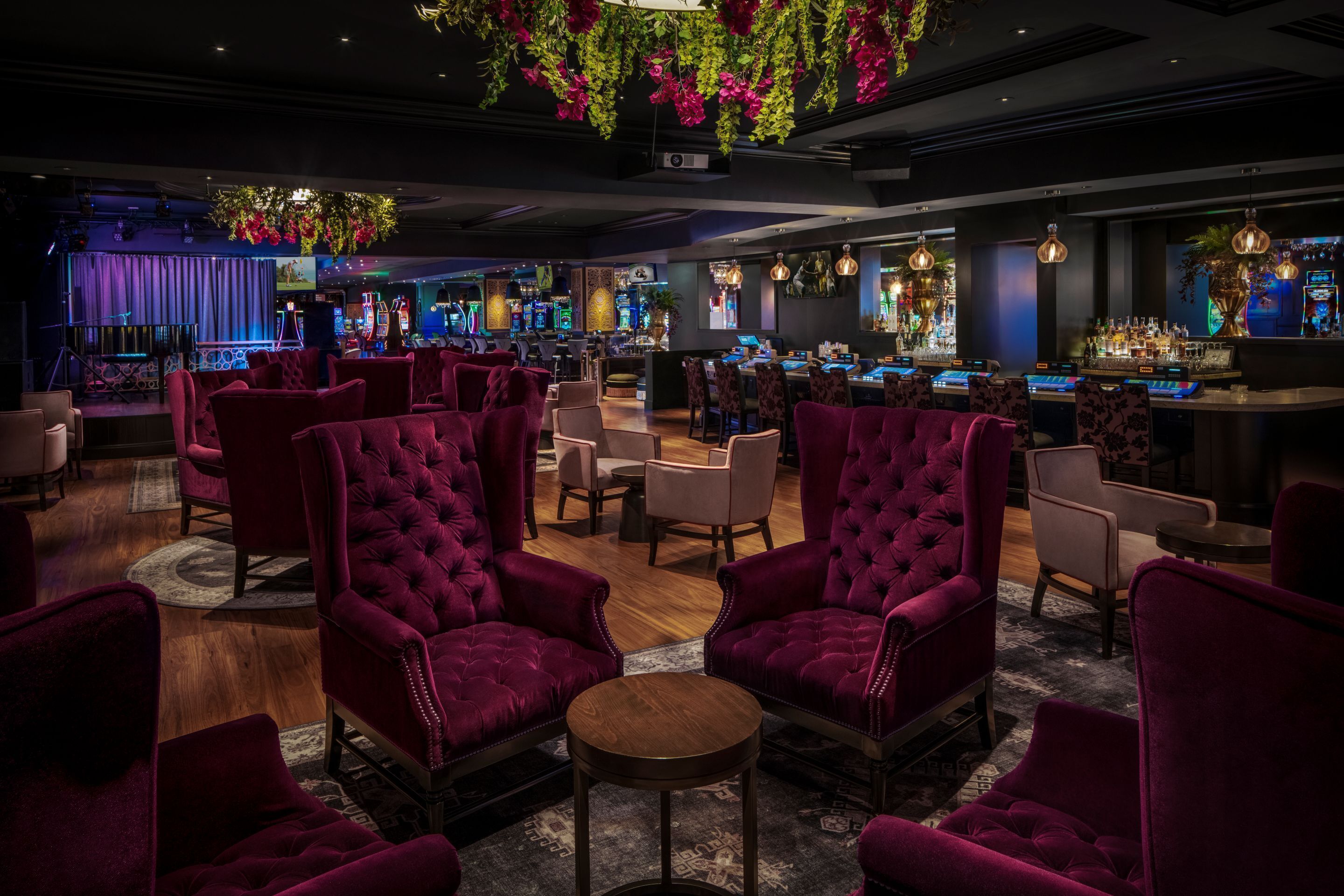 Zona de bar con asientos cómodos, un escenario y una barra con varias botellas y una pantalla de televisión.