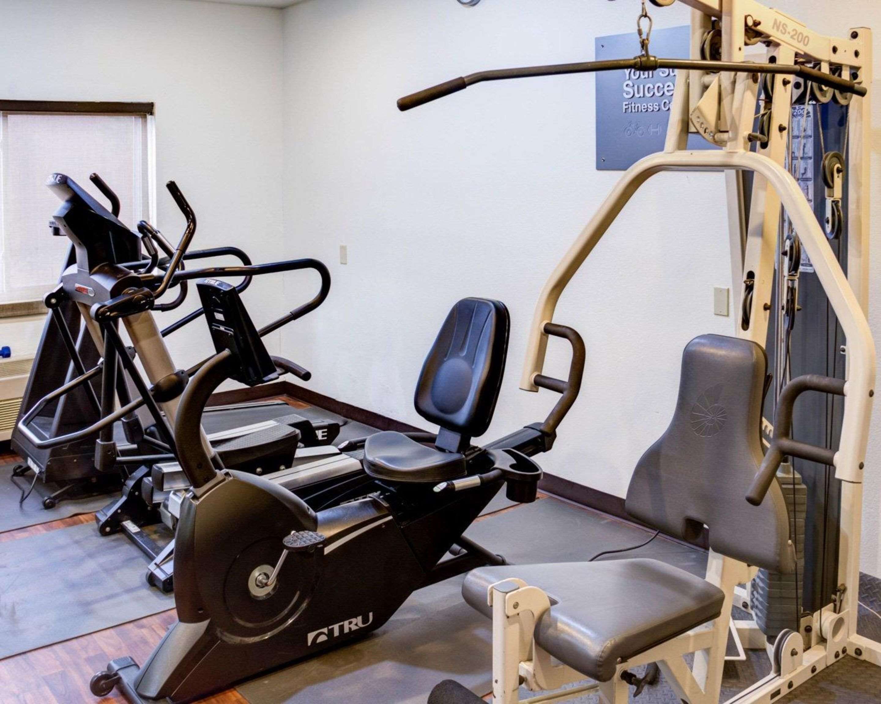 A gym with various exercise equipment including a TRU elliptical trainer, a weight bench, and a squat rack.