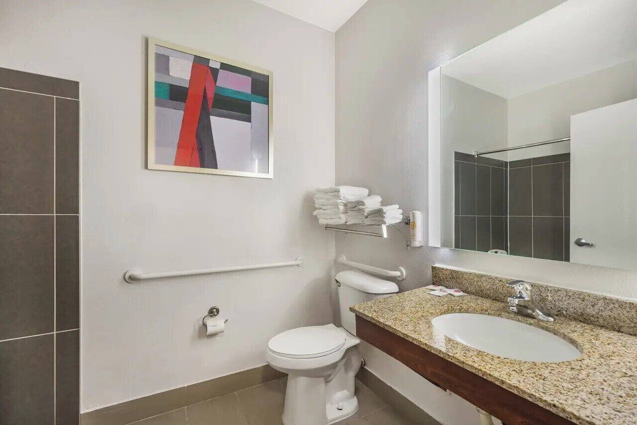 Un baño moderno con inodoro, lavamanos y barras de apoyo.