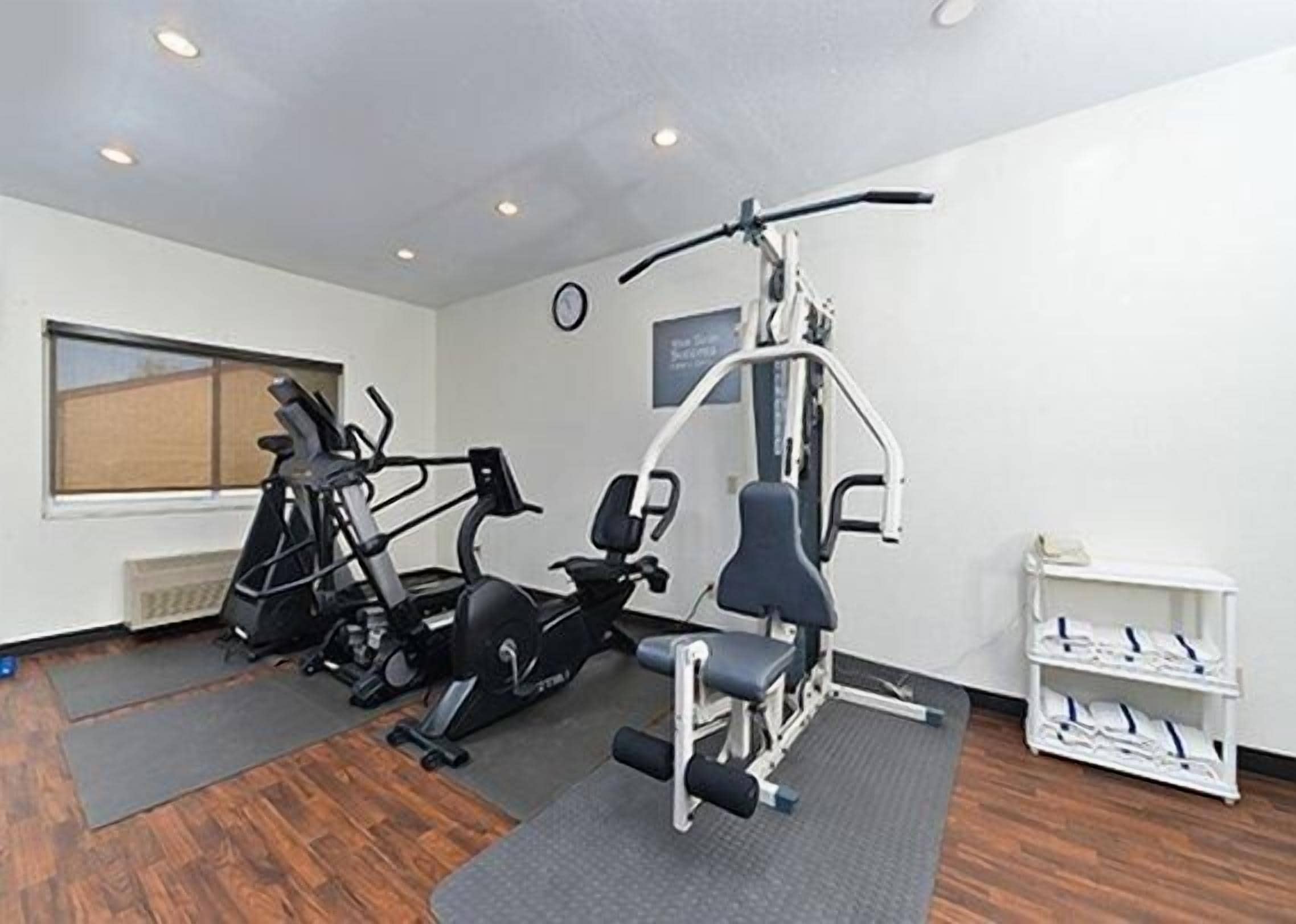 A gym with cardio machines, weight benches, and a wall-mounted clock.