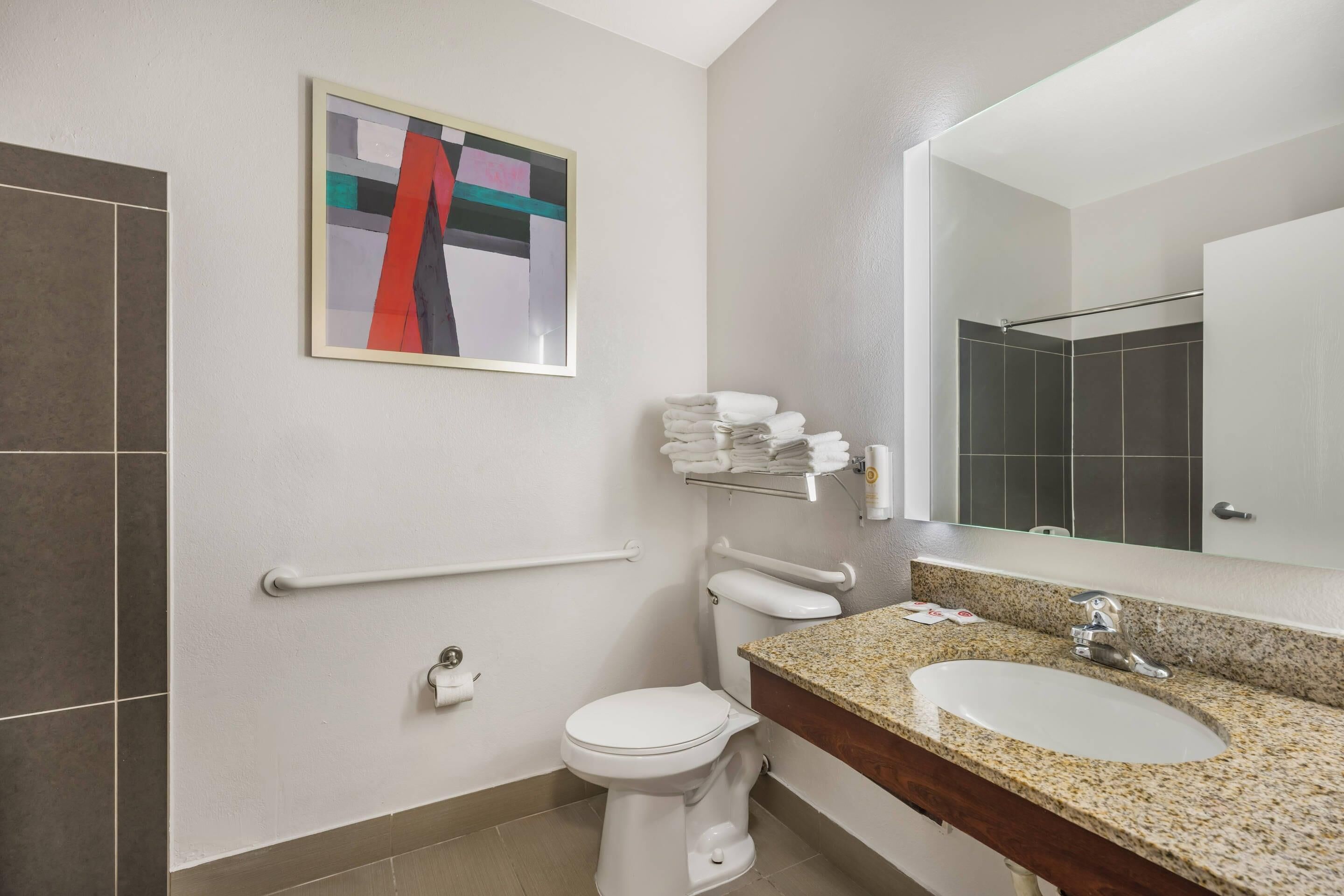 A modern bathroom with a toilet, sink, and handrails.