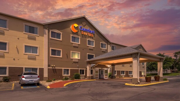 Un hotel Comfort Suites con entrada techada, estacionamiento y cielo al atardecer.