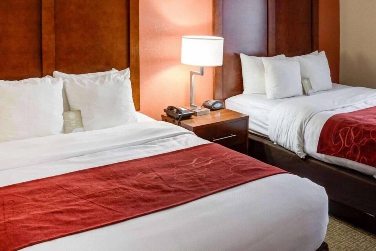 A hotel room with two beds, a nightstand with a lamp, and a wooden headboard.